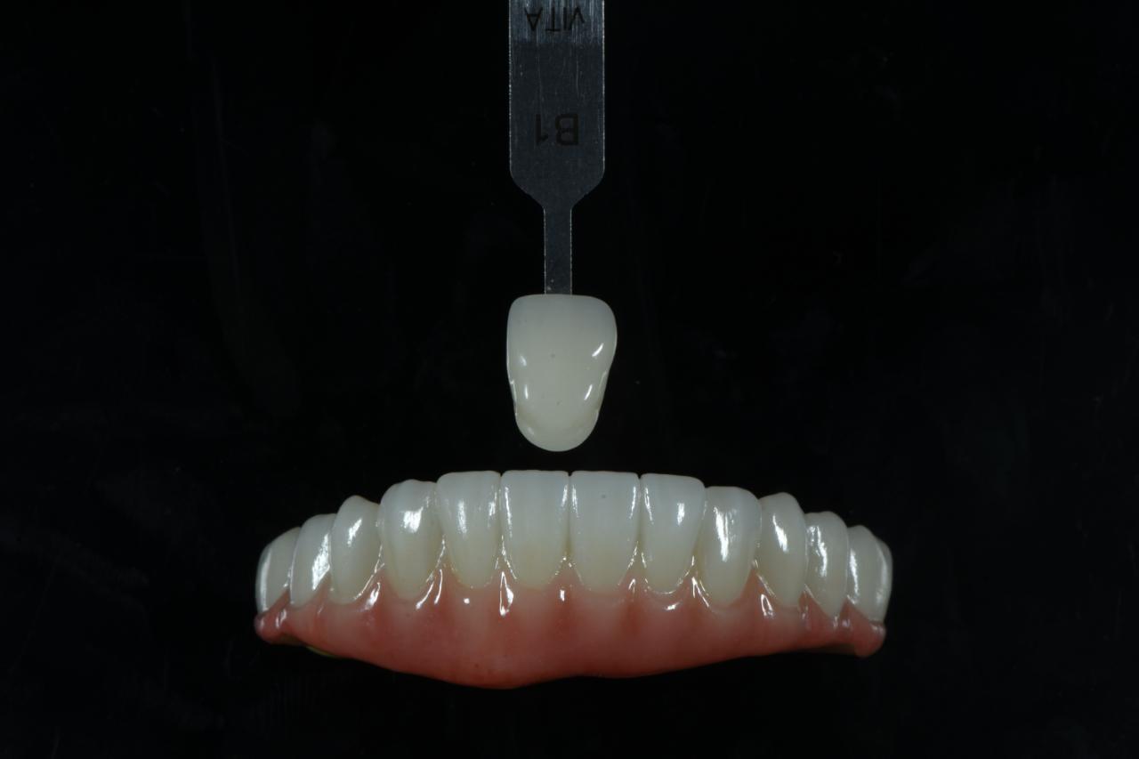 Hands finishing a dental prosthesis with a fine brush